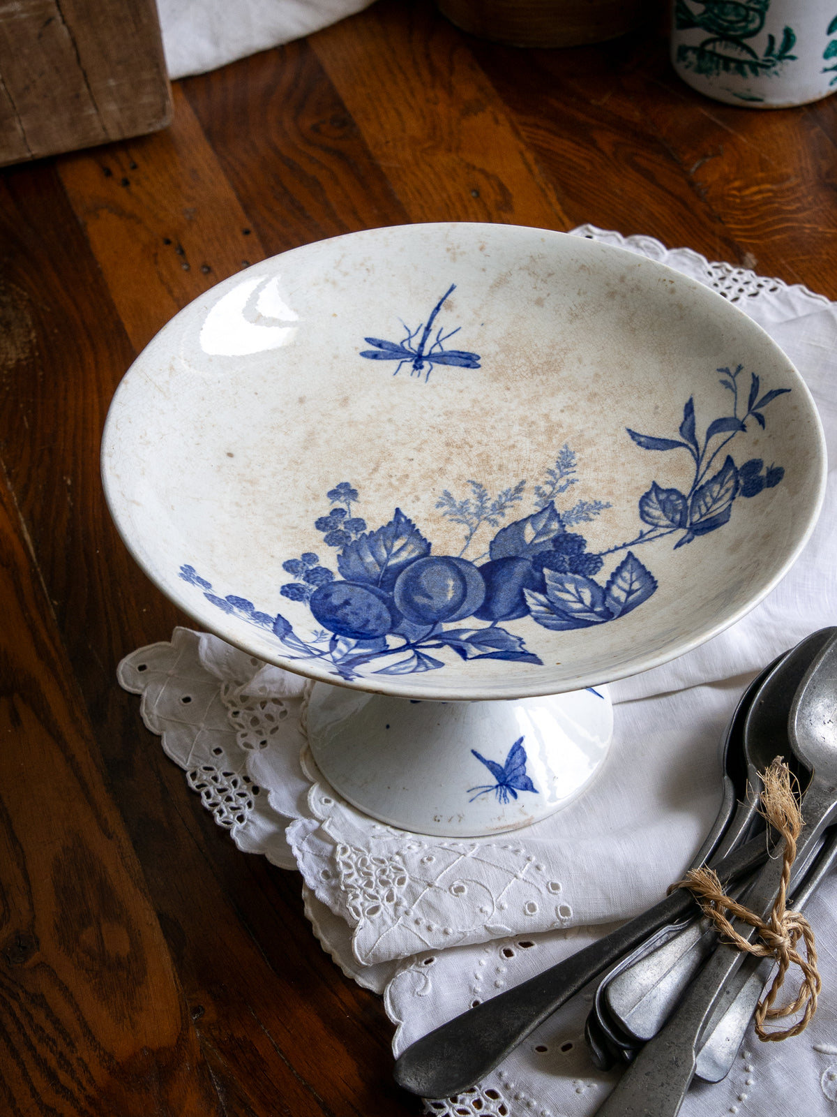 Compotier sur pied en faïence blanche ancienne française, orné d'un motif de libellule bleue et de fleurs. 