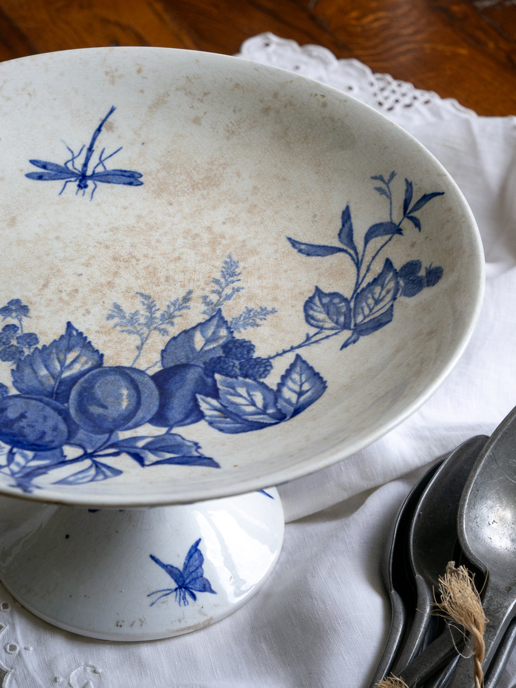 Compotier sur pied en faïence blanche ancienne française, orné d'un motif de libellule bleue et de fleurs. 