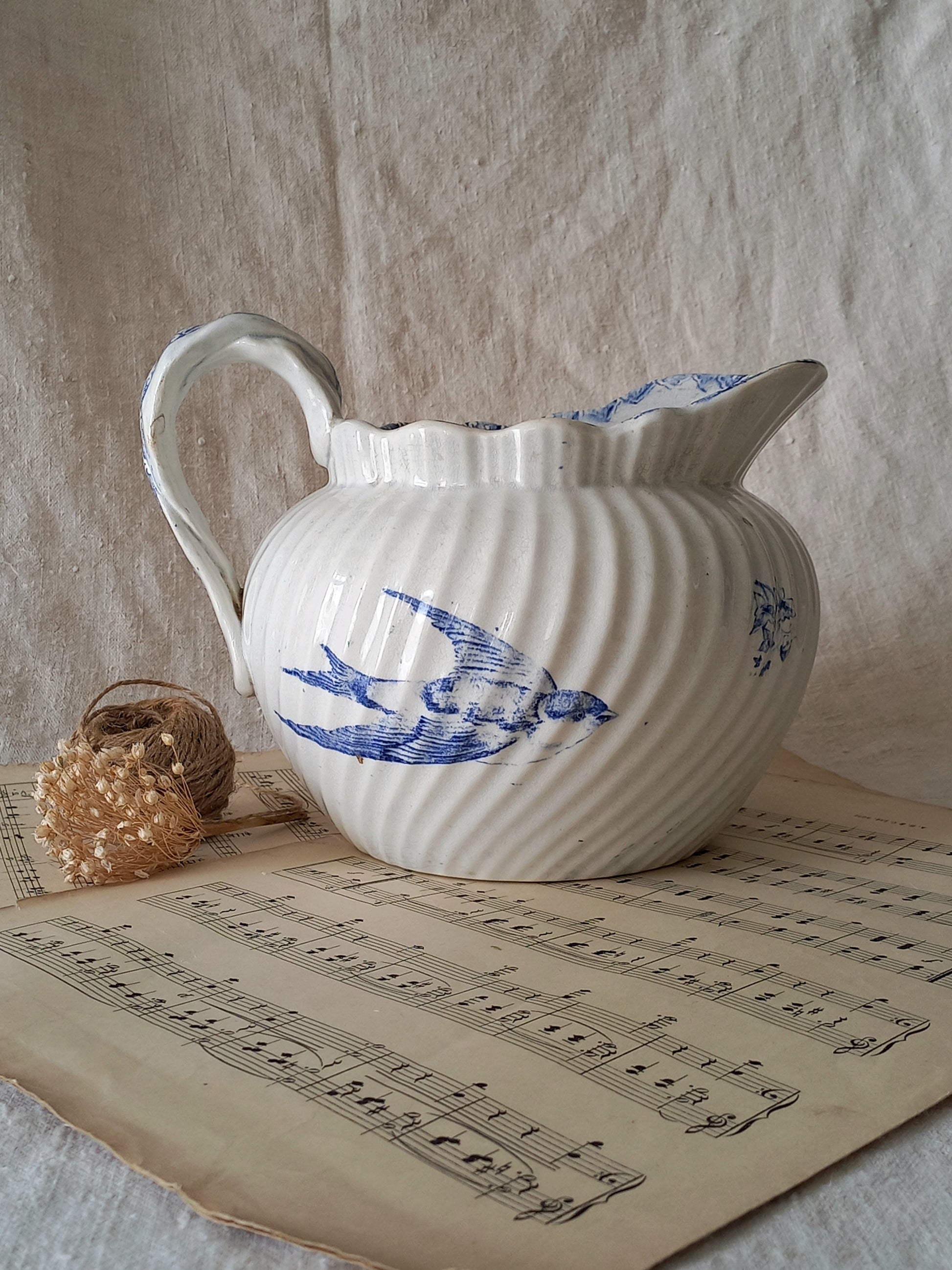 White ceramic pitcher with blue bird design on a sheet of music