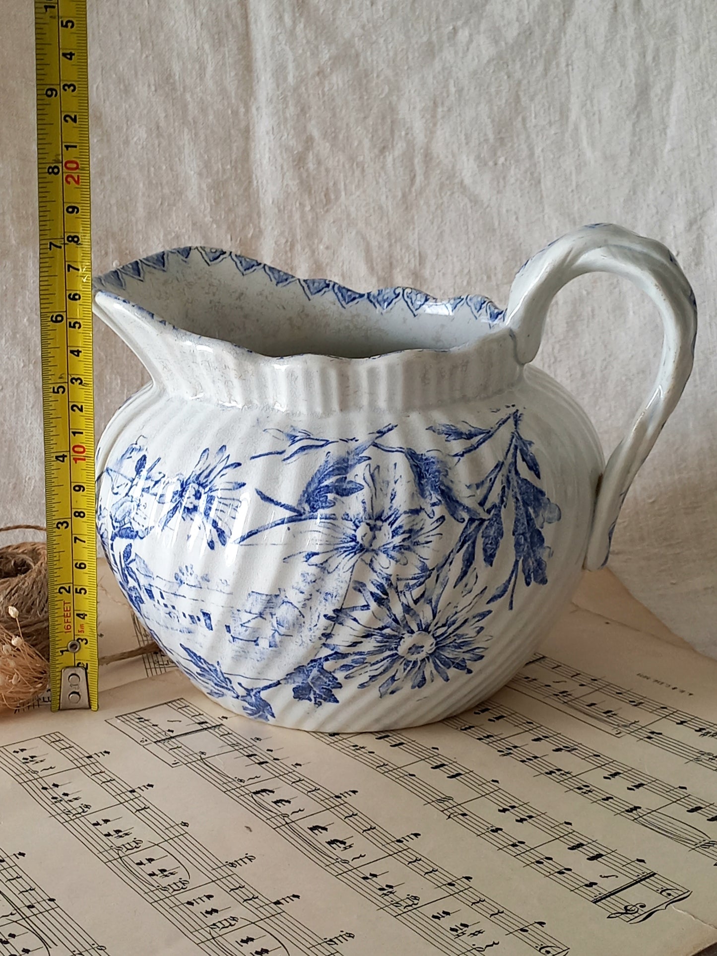 White ceramic pitcher with blue floral pattern on sheet music, with a ruler for scale.