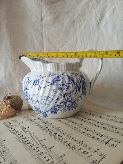 White ceramic pitcher with blue floral patterns on a sheet of music, measured by a yellow tape measure.