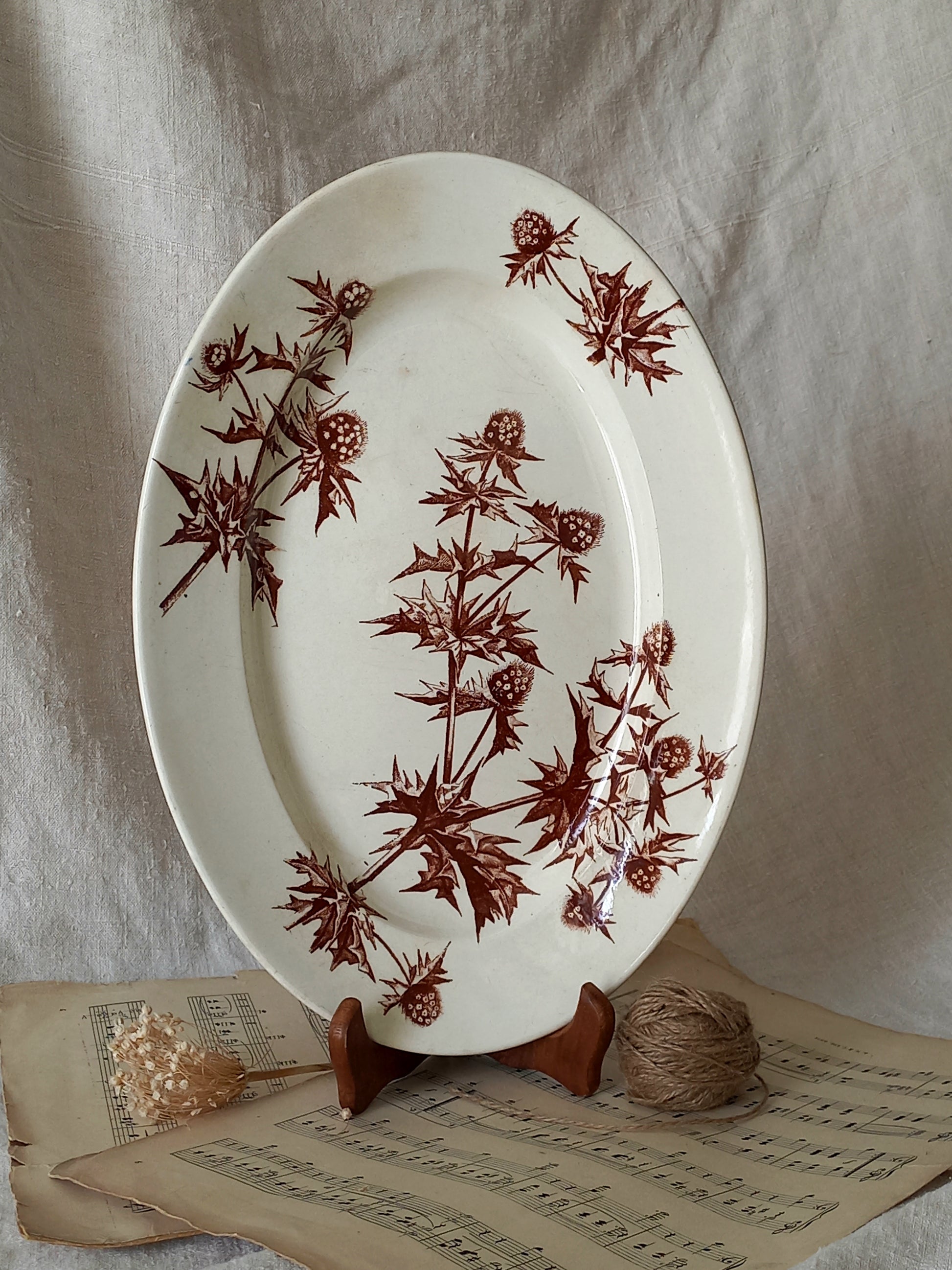 Oval ceramic plate with brown floral pattern on a stand, placed on sheet music.