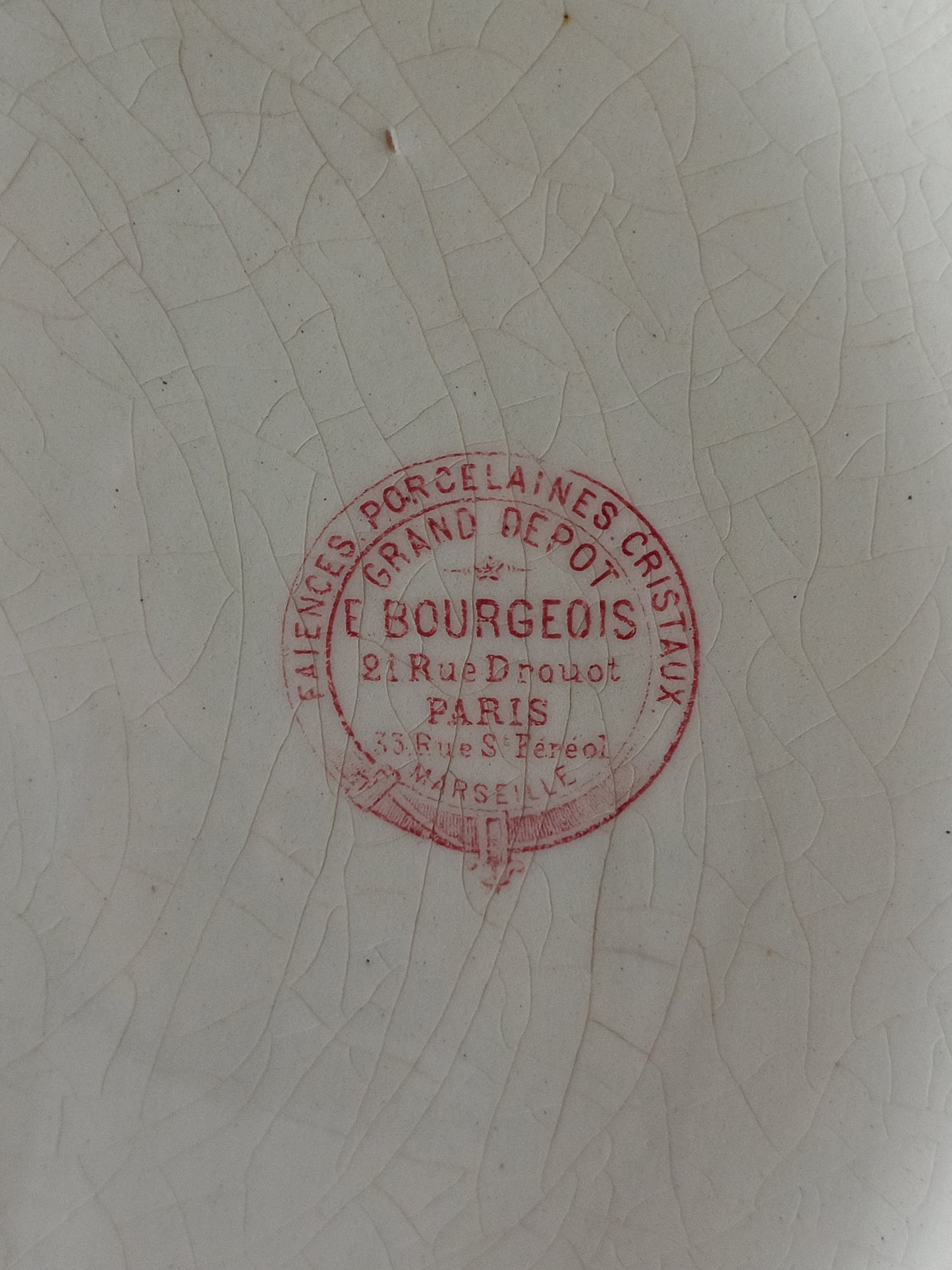 A close-up of a white porcelain surface with a circular red stamp reading E. Bourgeois, Paris