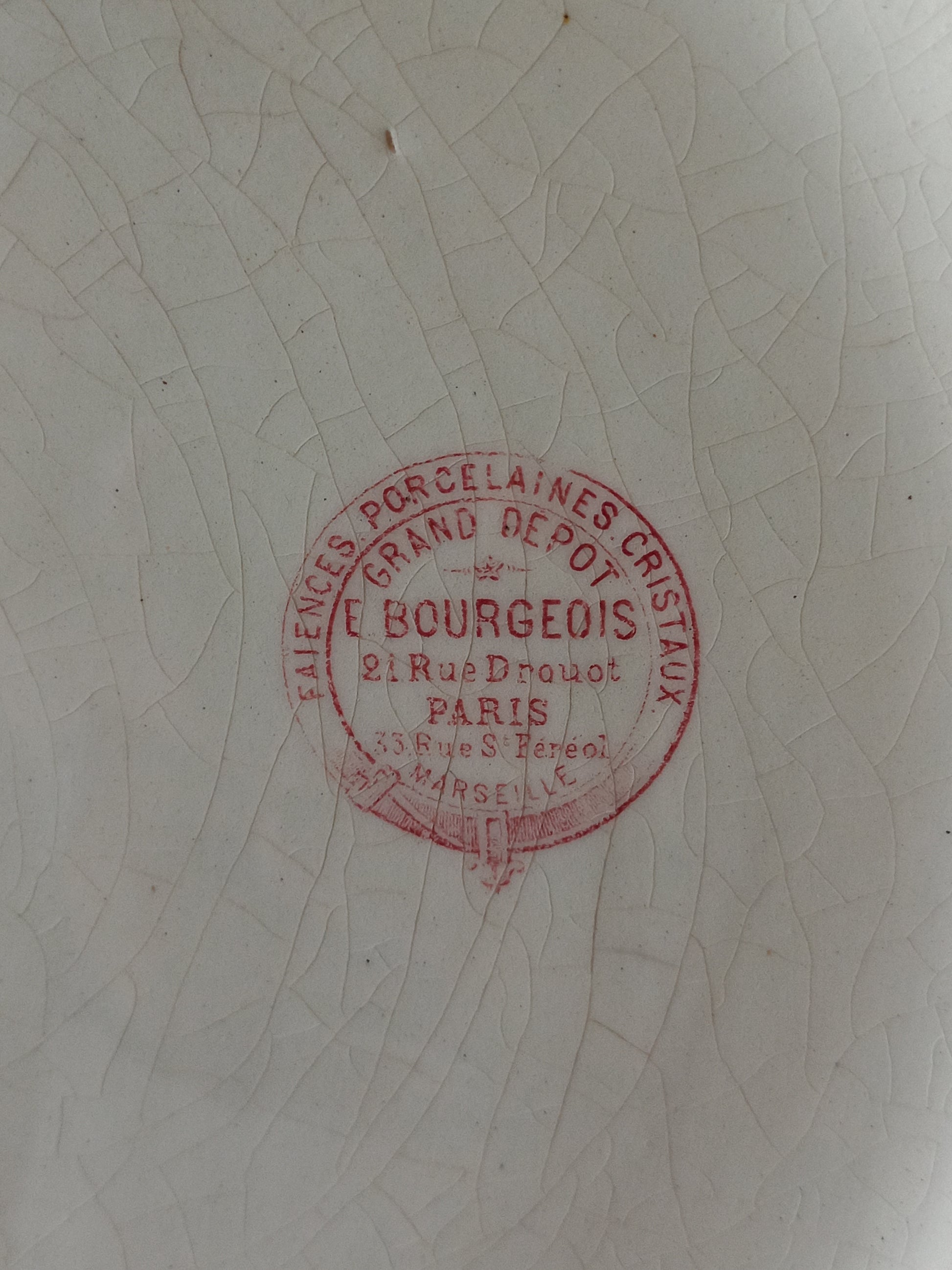 A close-up of a white porcelain surface with a circular red stamp reading E. Bourgeois, Paris