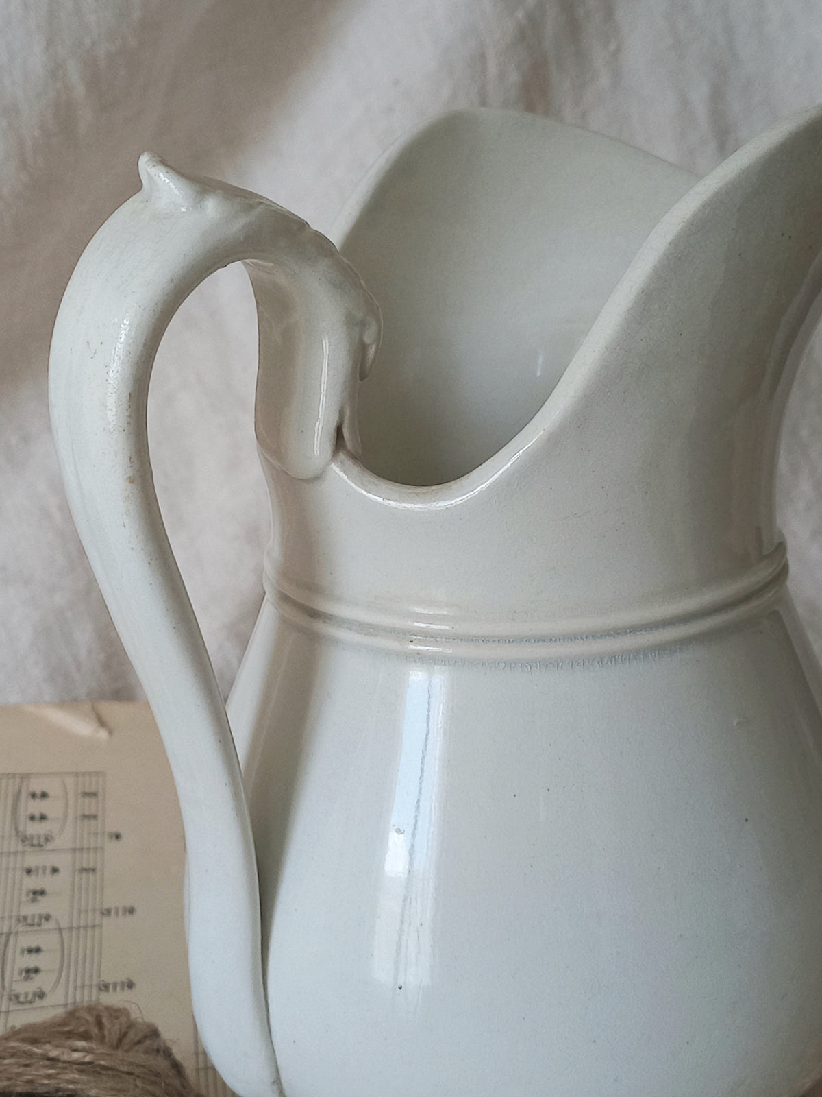 Close-up of a French antique white ironstone jug or pitcher with swan neck handle in a decorative setting.