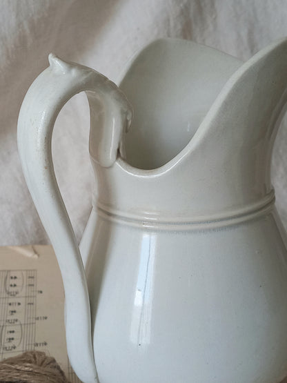 Close-up of a French antique white ironstone jug or pitcher with swan neck handle in a decorative setting.