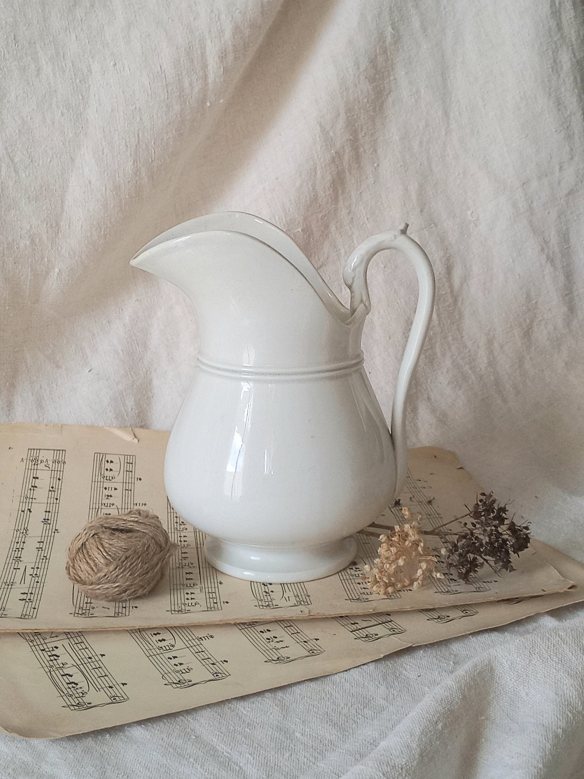 French antique white ironstone jug or pitcher with swan neck handle in a decorative setting.