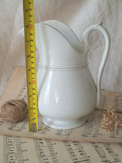 Close-up of a French antique white ironstone jug or pitcher with swan neck handle in a decorative setting.