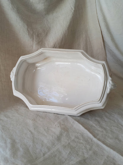 Interior of an antique white ceramic planter with a lion head relief on the front and claw-footed base, set against a draped beige fabric background.