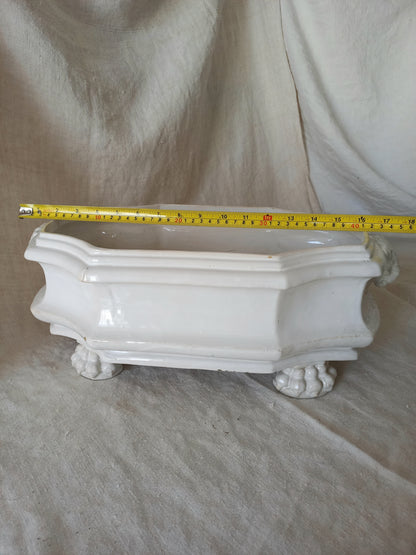 antique white ceramic planter with a lion head relief on the front and claw-footed base, set against a draped beige fabric background with tape measure for reference.
