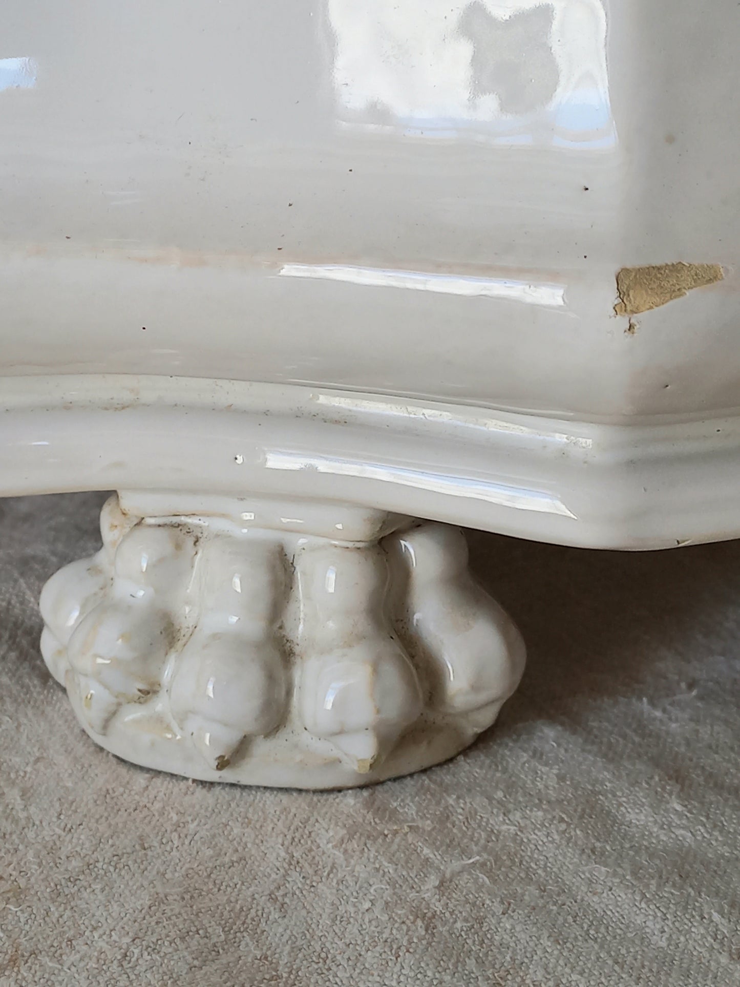 Close-up of an antique white ceramic planter with a decorative ribbed pedestal base, resting on a textured beige fabric surface.
