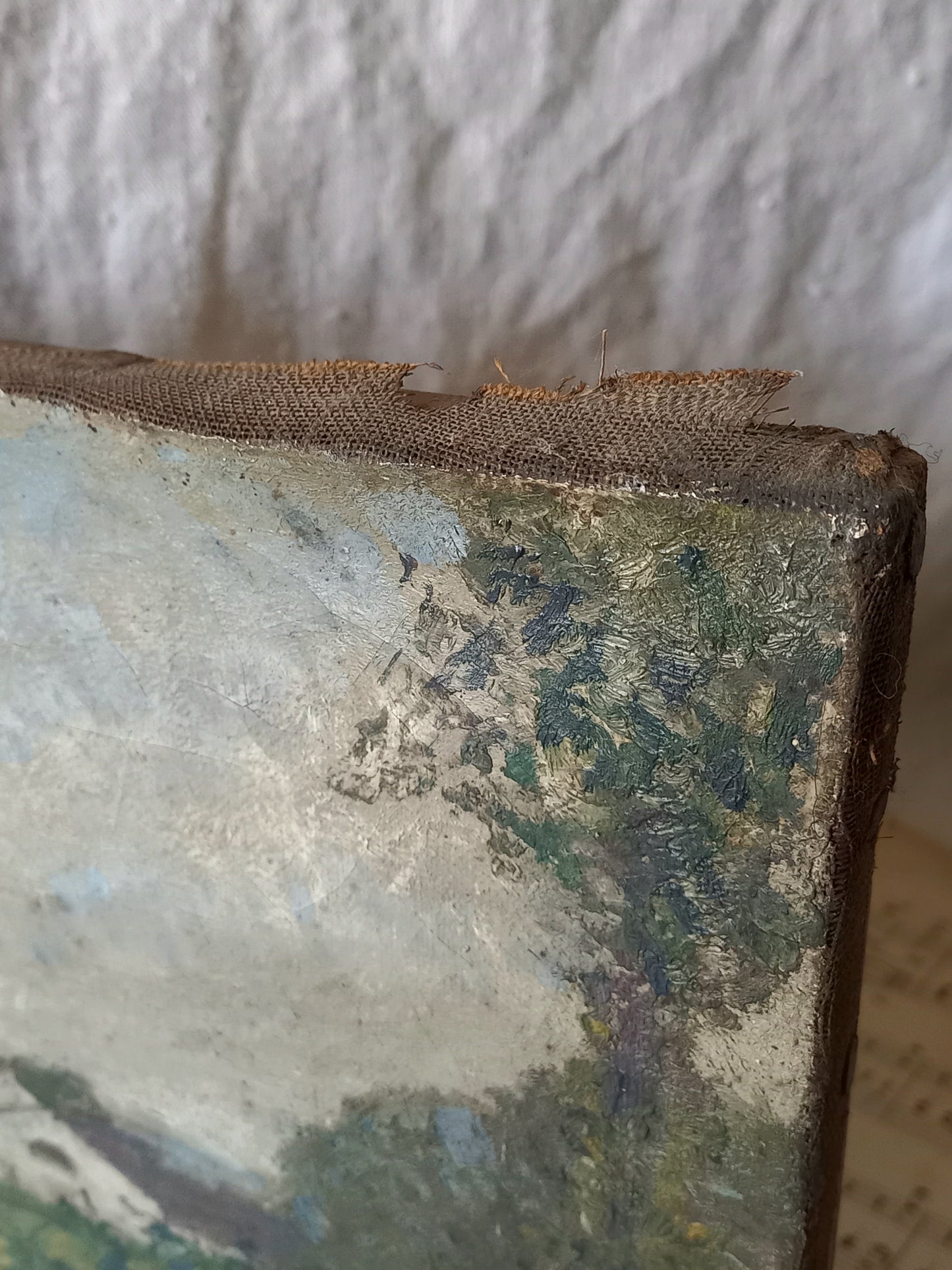 Close-up of a distressed canvas painting showing the rough, textured edge with peeling paint and a frayed fabric strip along the top, set against a neutral background.