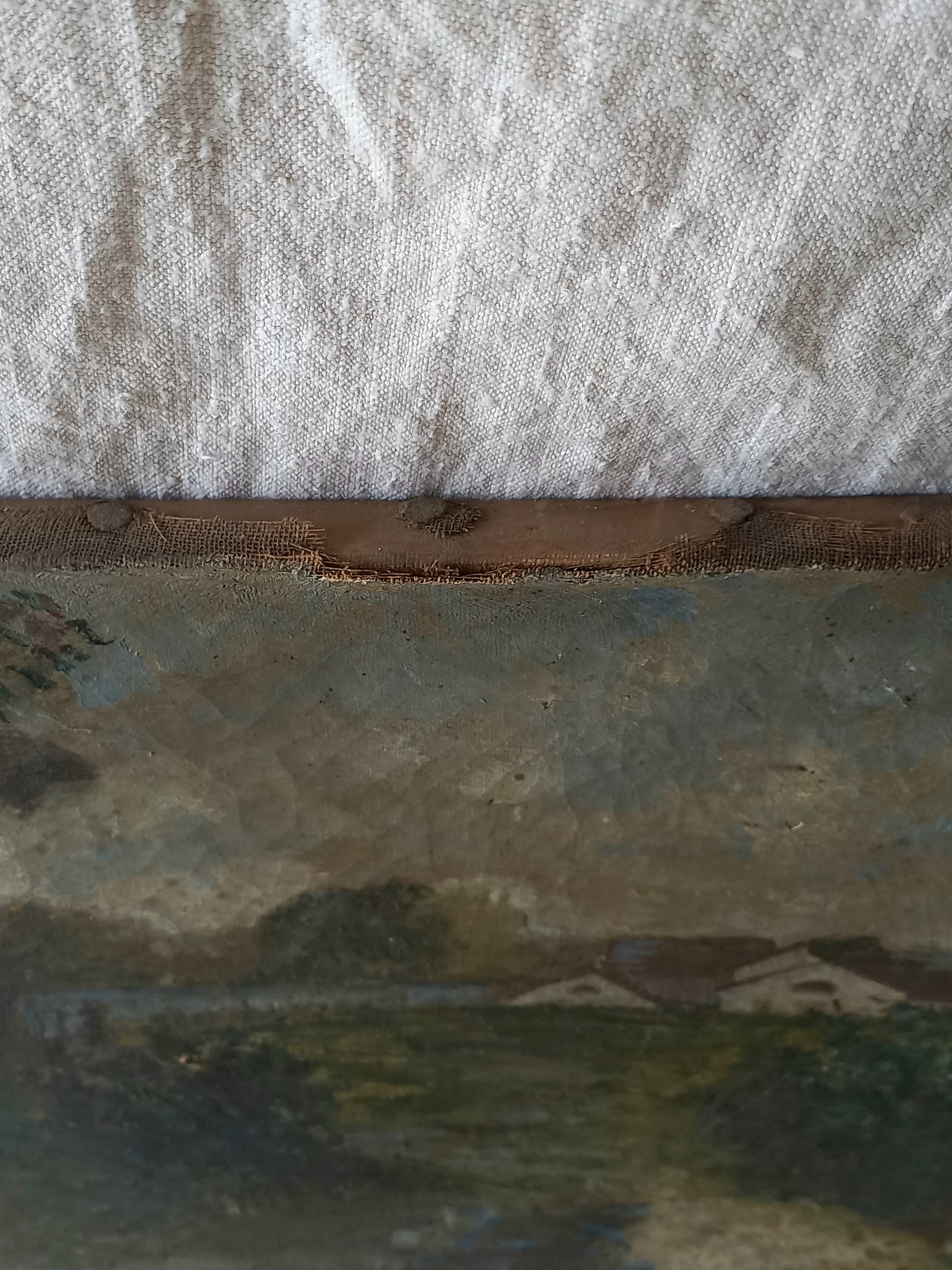 A close-up detail of an antique landscape painting showing textured canvas, a rustic wooden edge, and a textured off-white fabric background.
