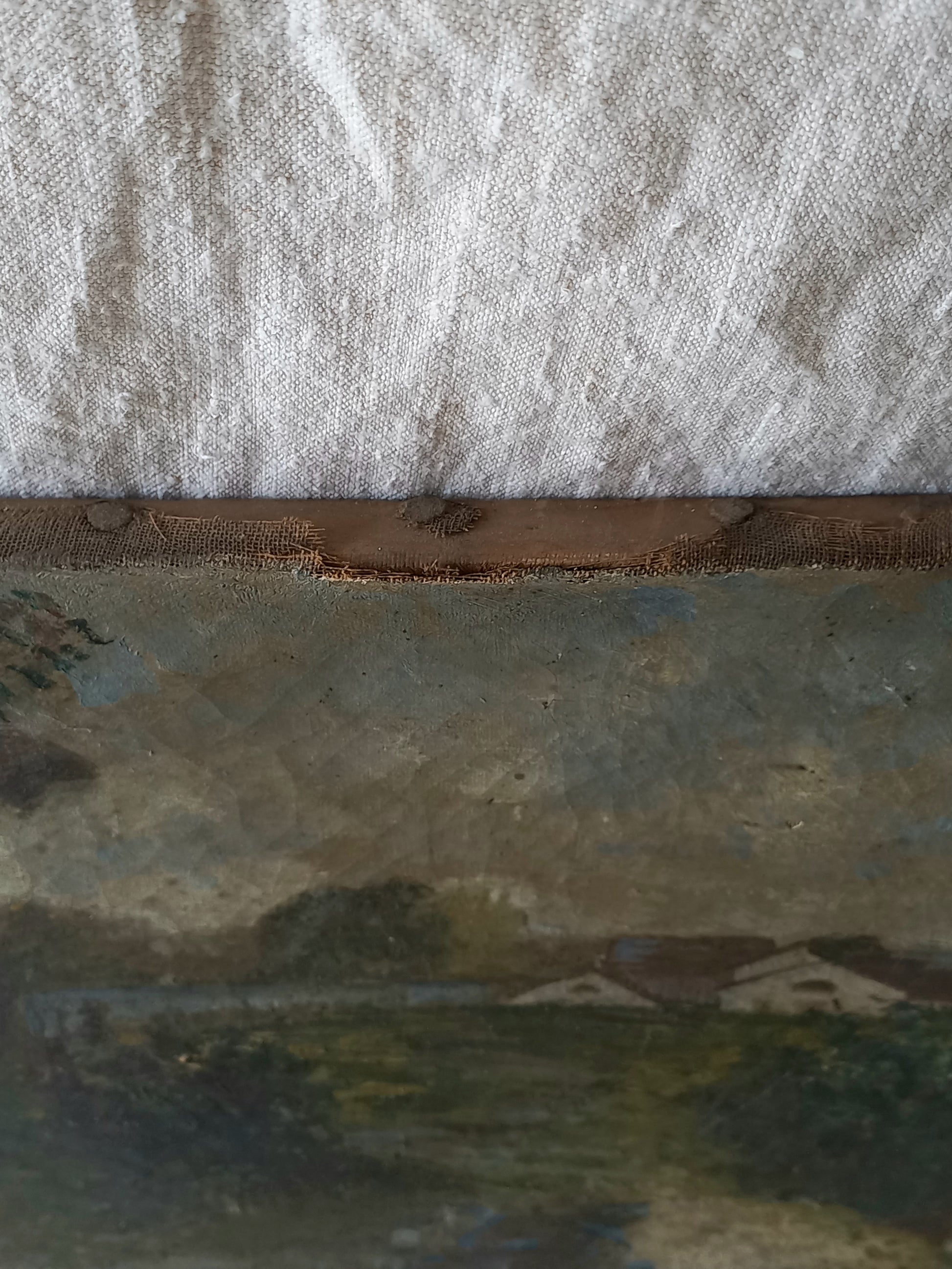 A close-up detail of an antique landscape painting showing textured canvas, a rustic wooden edge, and a textured off-white fabric background.