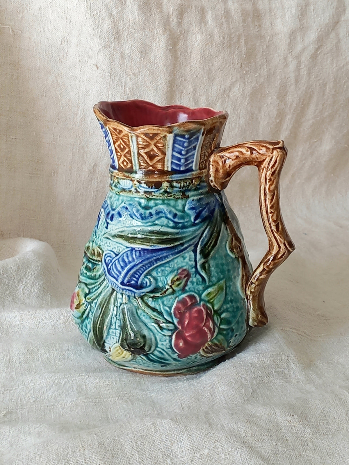 An antique majolica pitcher with a rich glaze set against a draped white fabric background.