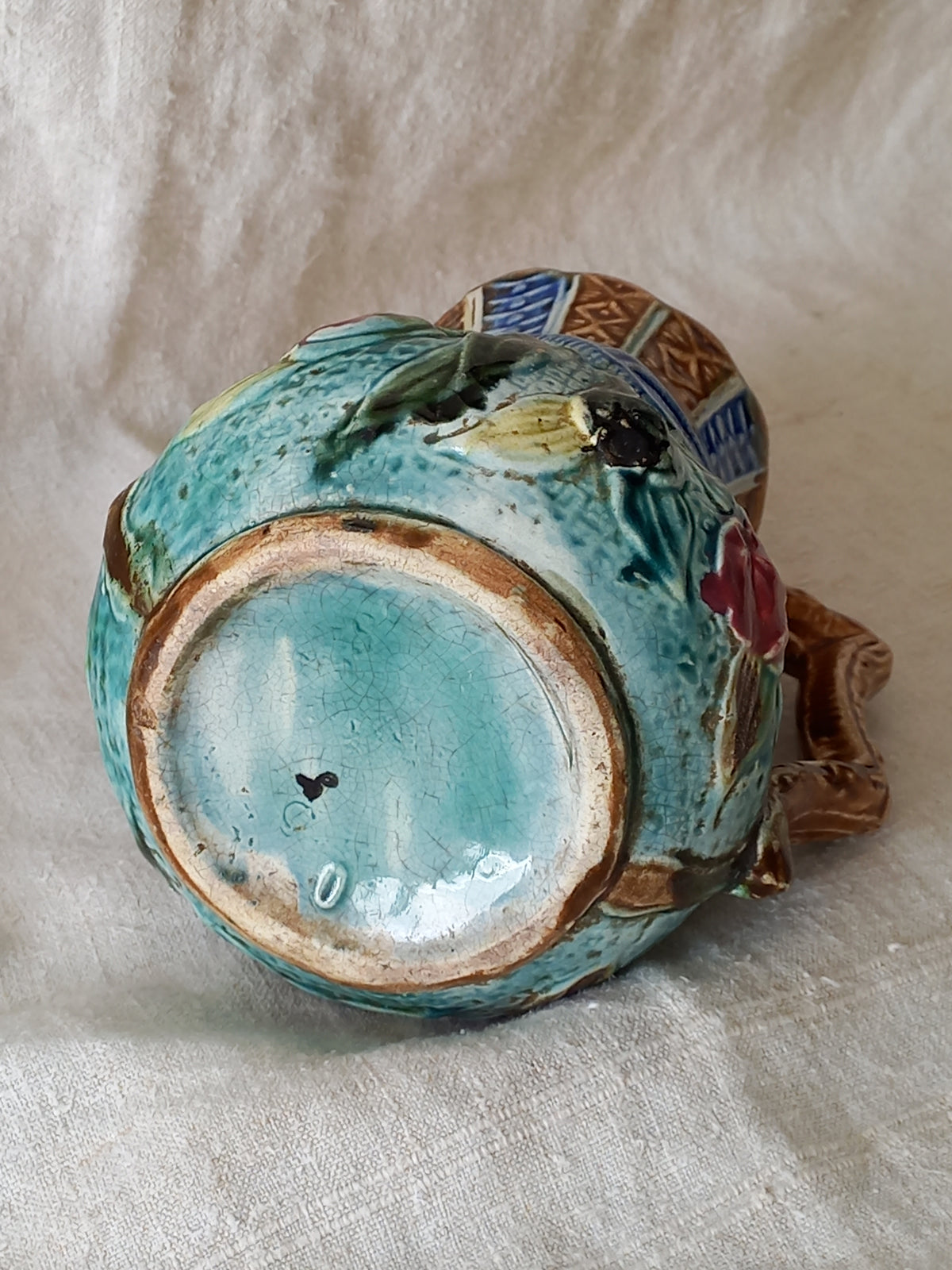 Underside of an antique majolica pitcher with a rich glaze set against a draped white fabric background.