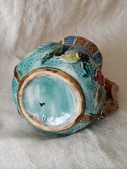 Underside of an antique majolica pitcher with a rich glaze set against a draped white fabric background.