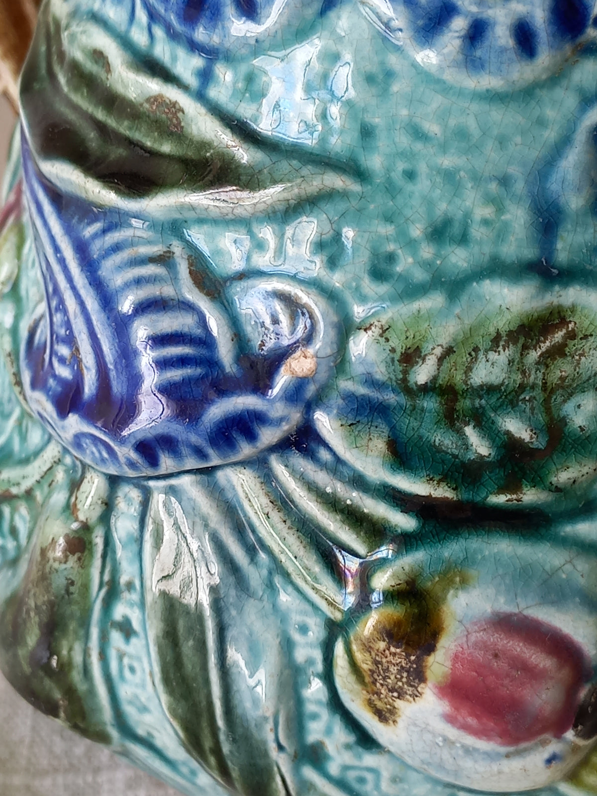 Close-up of an antique majolica pitcher with a rich glaze set against a draped white fabric background.