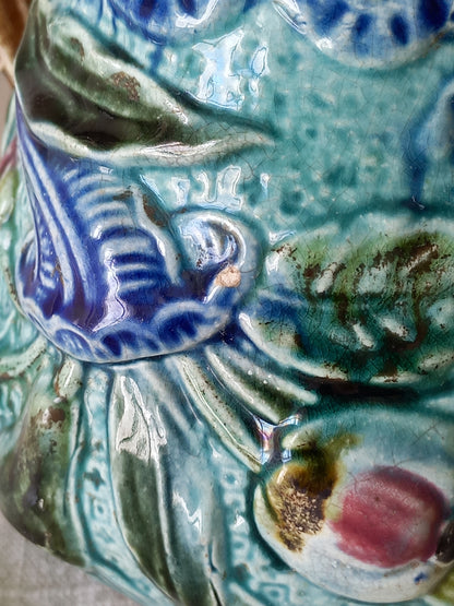 Close-up of an antique majolica pitcher with a rich glaze set against a draped white fabric background.