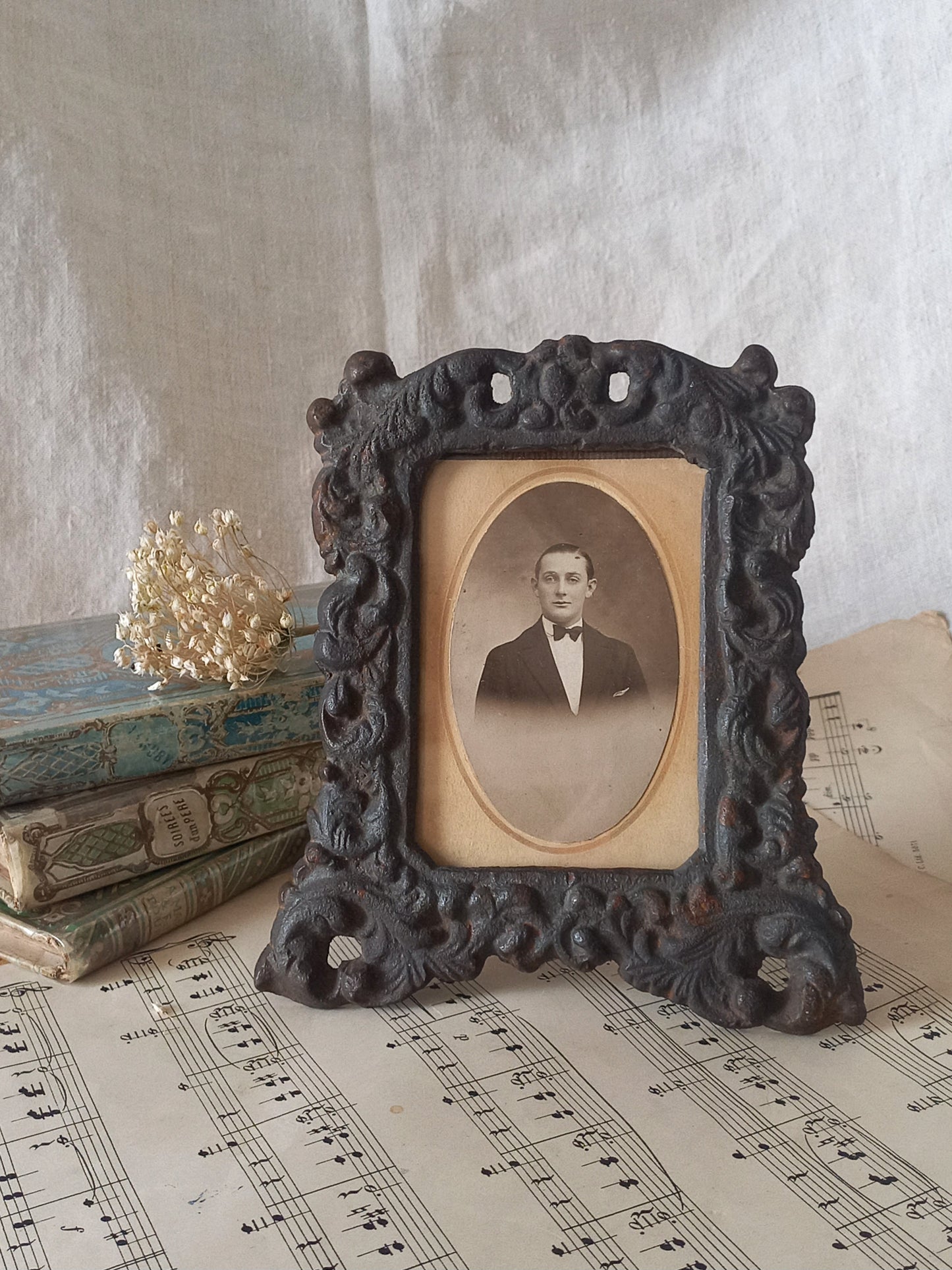 A small French antique decorative cast iron photo frame with time-worn patina. There is a glass front and a hardboard backing board. Inside is an original period photo.