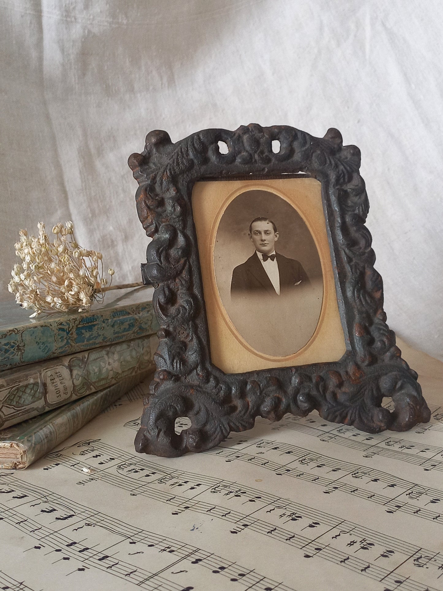 A small French antique decorative cast iron photo frame with time-worn patina. There is a glass front and a hardboard backing board. Inside is an original period photo.