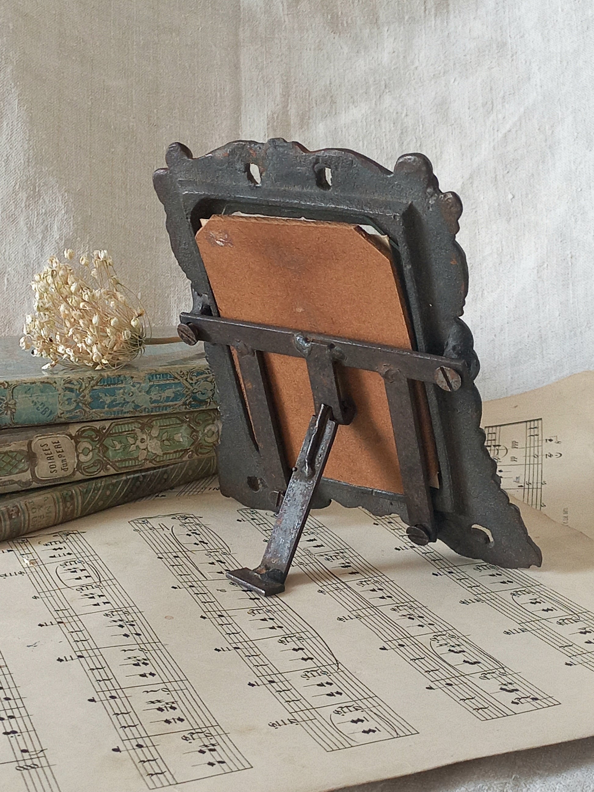 A small French antique decorative cast iron photo frame with time-worn patina. There is a glass front and a hardboard backing board. Inside is an original period photo.