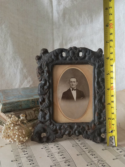 A small French antique decorative cast iron photo frame with time-worn patina. There is a glass front and a hardboard backing board. Inside is an original period photo.