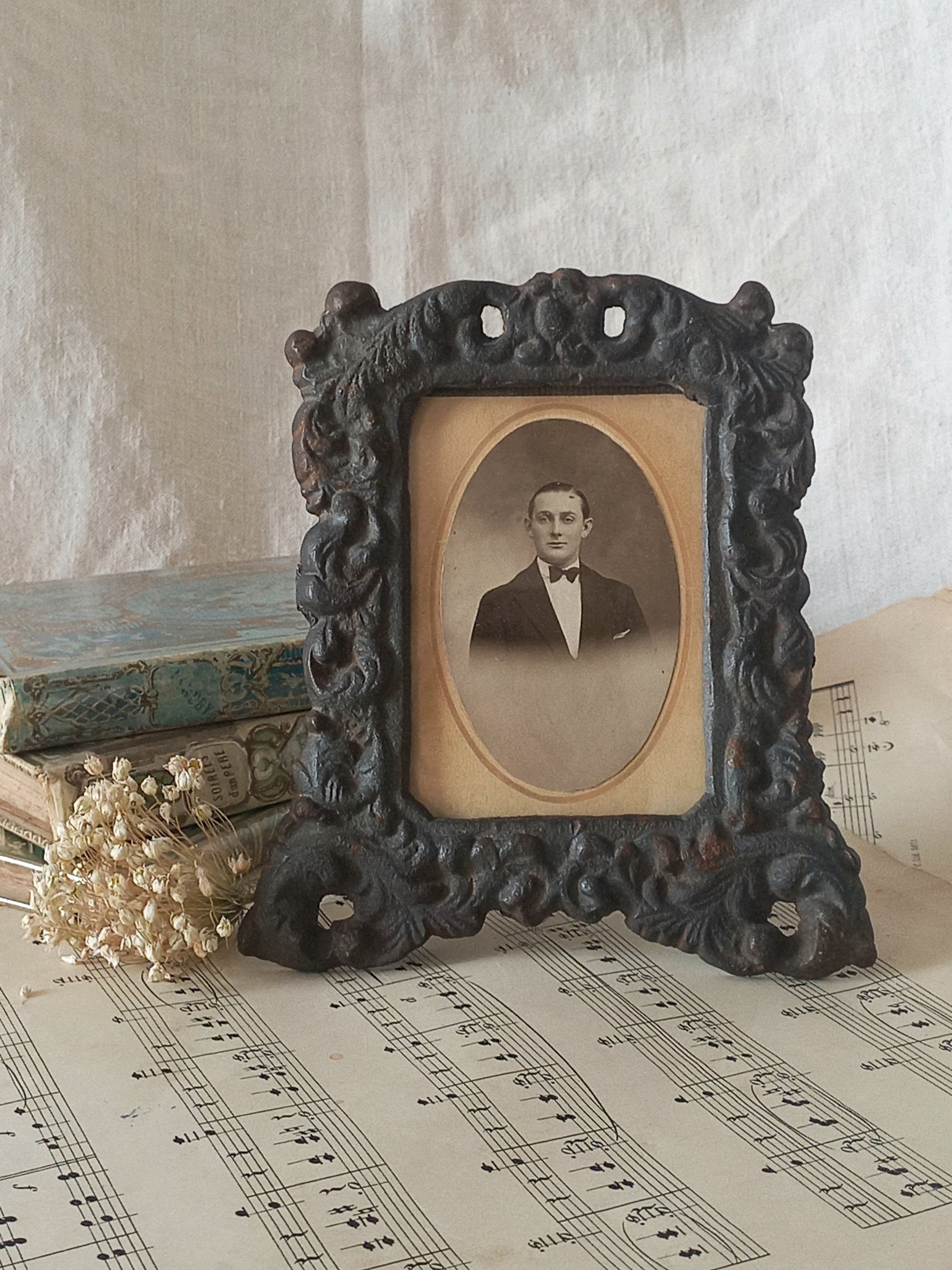 A small French antique decorative cast iron photo frame with time-worn patina. There is a glass front and a hardboard backing board. Inside is an original period photo.