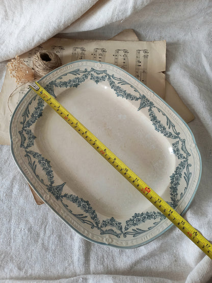Antique ceramic platter with decorative border on a white fabric background, measured with a tape measure.