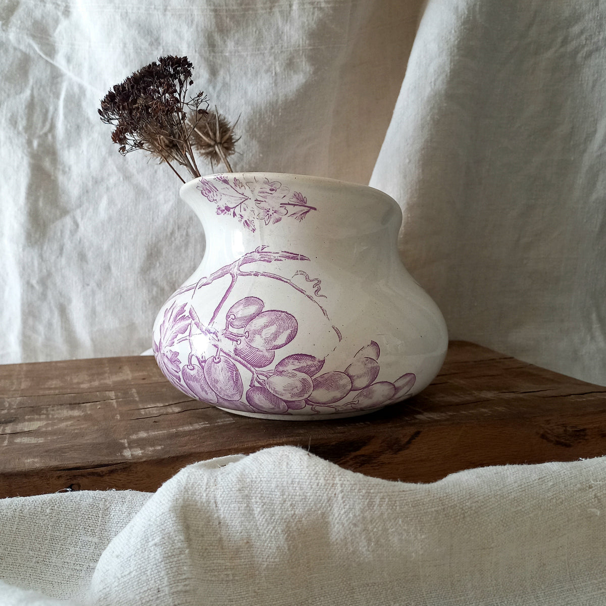 White vase with purple floral patterns on a wooden surface with a white fabric background