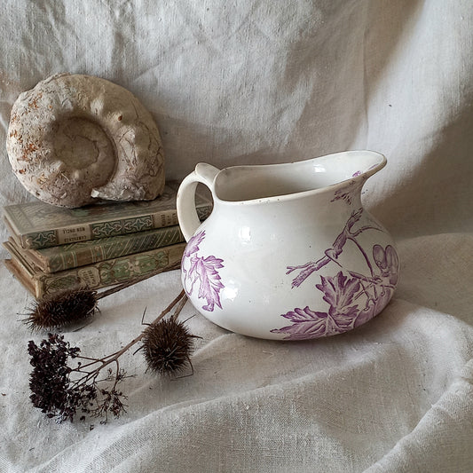White ceramic pitcher with purple floral design on a textured fabric background