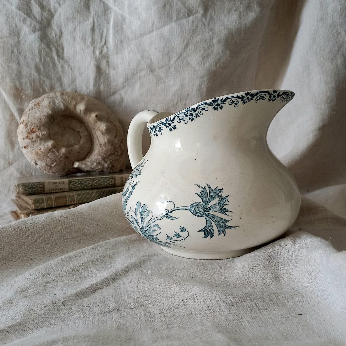 White ceramic pitcher with teal floral patterns on a textured fabric background