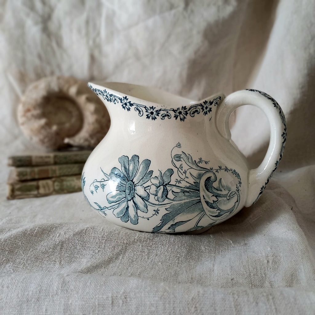 White ceramic pitcher with teal floral patterns on a textured fabric background