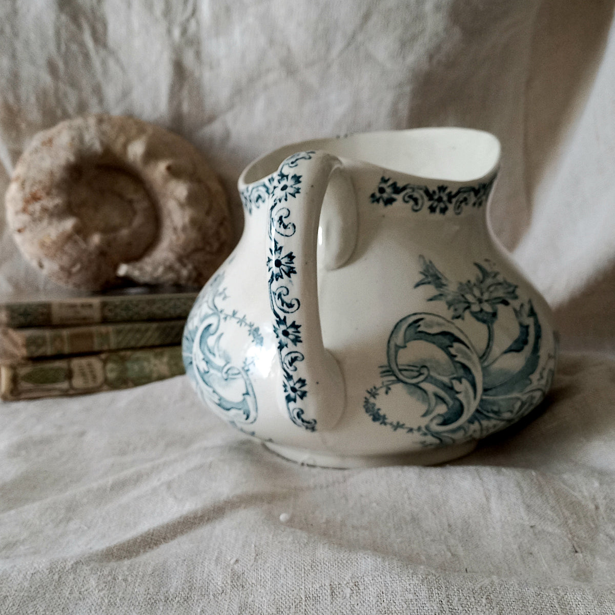 Ceramic pitcher with teal floral patterns on a textured surface