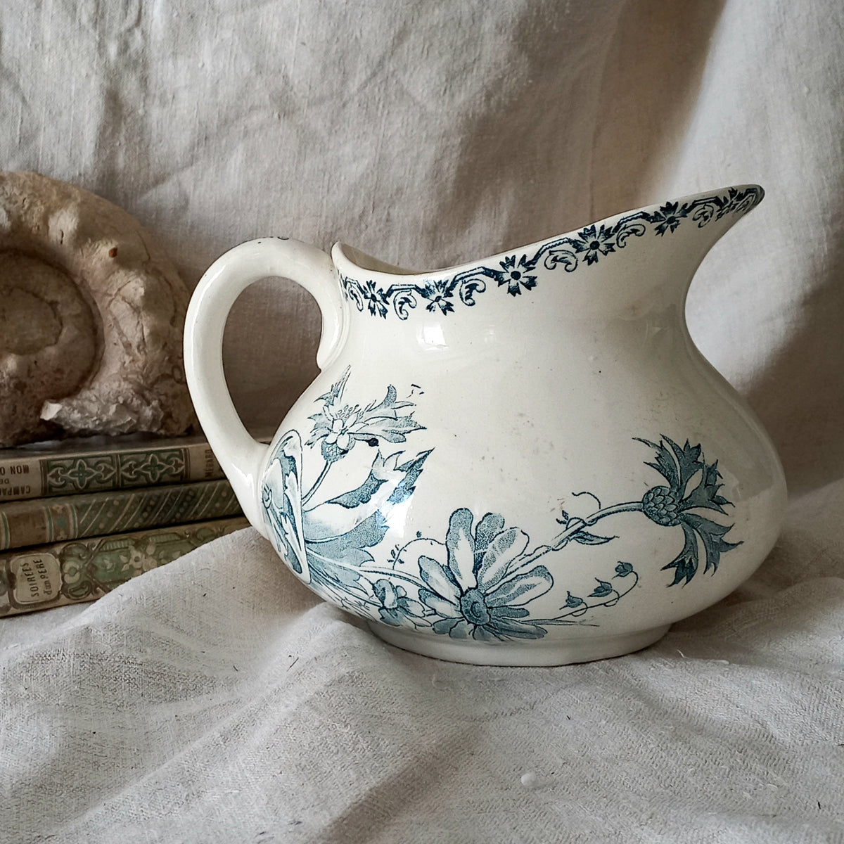 White ceramic pitcher with teal floral patterns on a textured surface