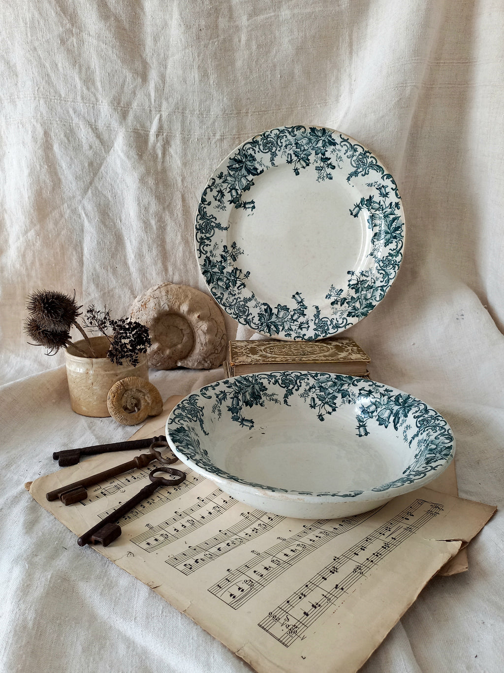 Floral-patterned ceramic plates and bowl on a textured fabric background with vintage keys and sheet music.