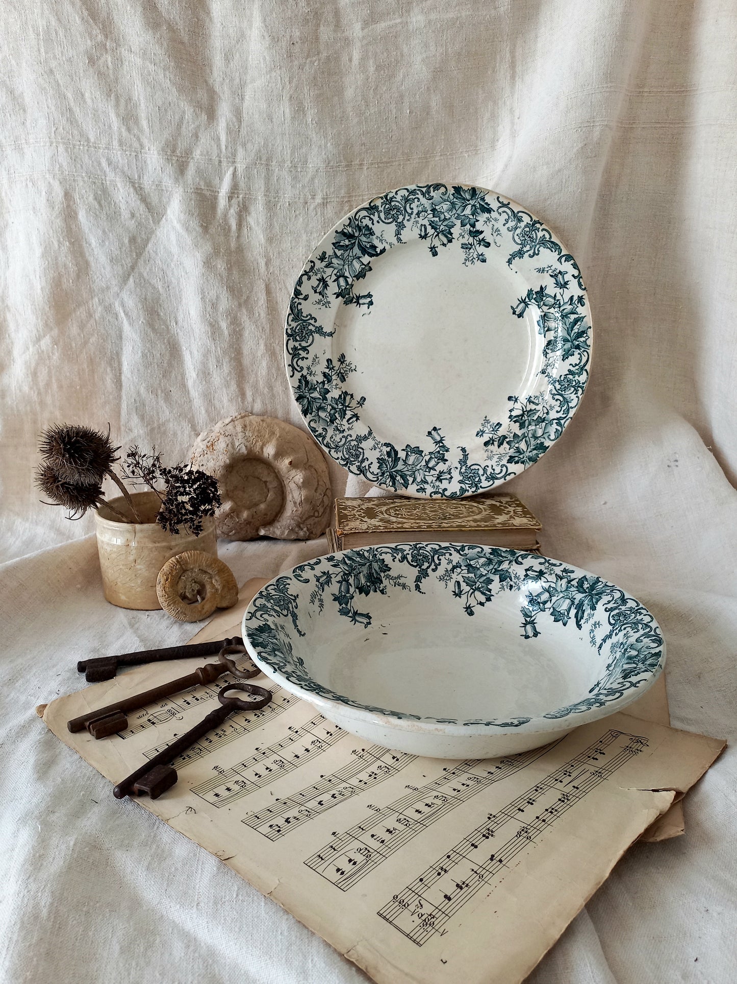 Floral-patterned ceramic plates and bowl on a textured fabric background with vintage keys and sheet music.
