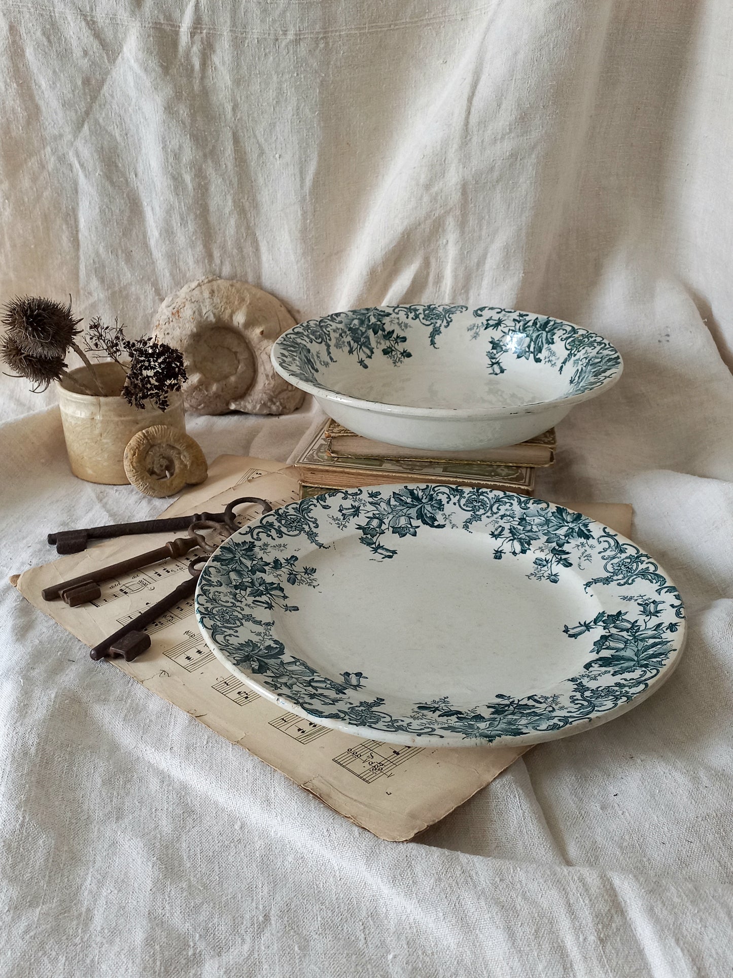 Two decorative plates with green floral patterns on a white fabric background.