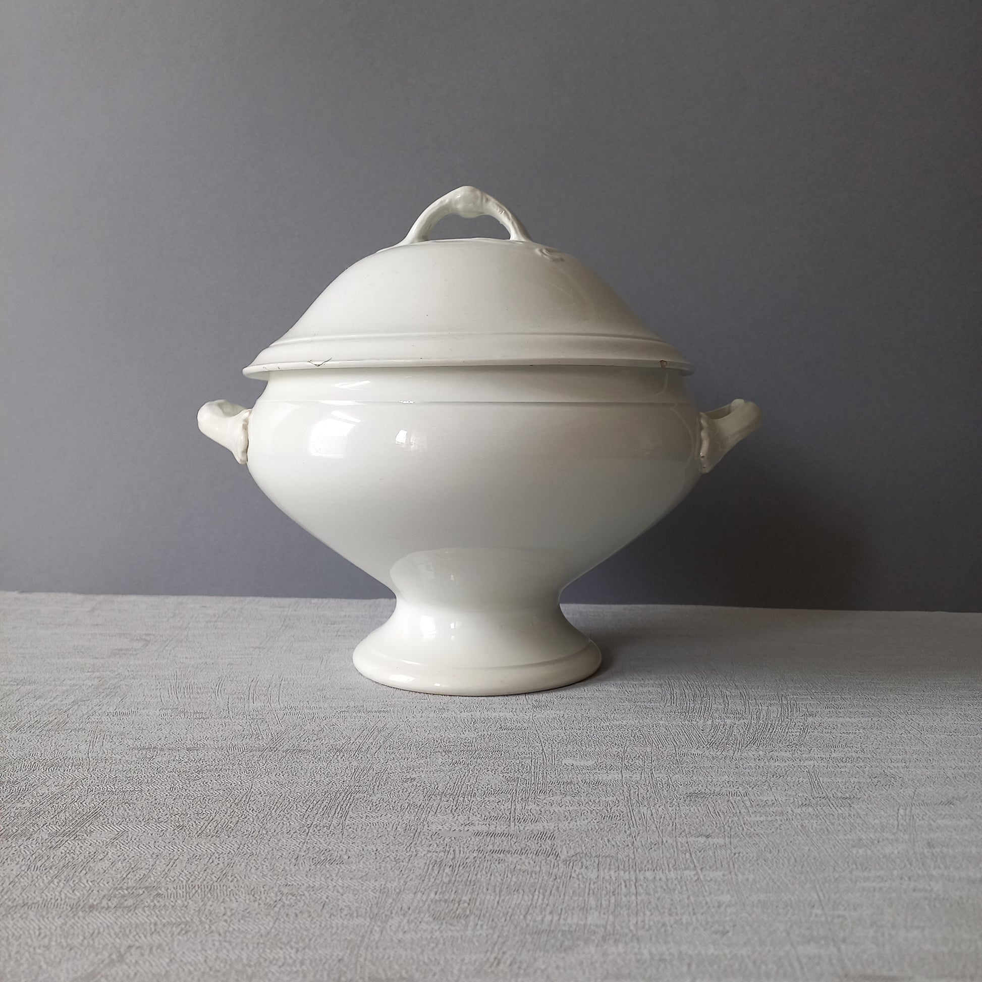 A small sized antique white ironstone soup tureen with elegant curves by French manufacturer Saint Amand et Hamage. This lovely old tureen has beautiful detailed handles either side of the tureen and on the lid. Circa late 19th to early 20th century.