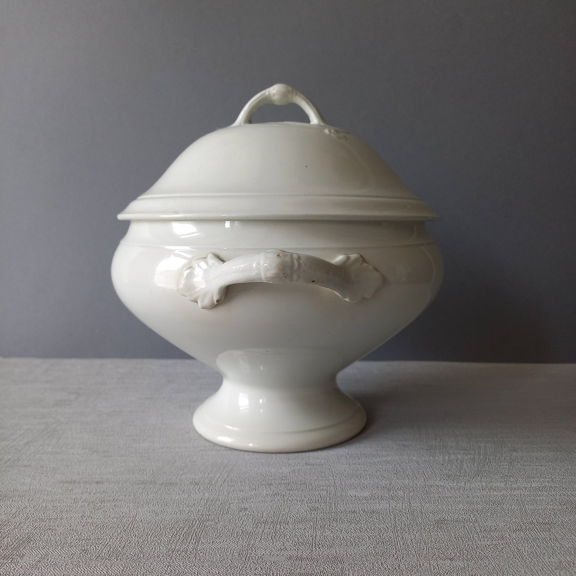 A small sized antique white ironstone soup tureen with elegant curves by French manufacturer Saint Amand et Hamage. This lovely old tureen has beautiful detailed handles either side of the tureen and on the lid. Circa late 19th to early 20th century.