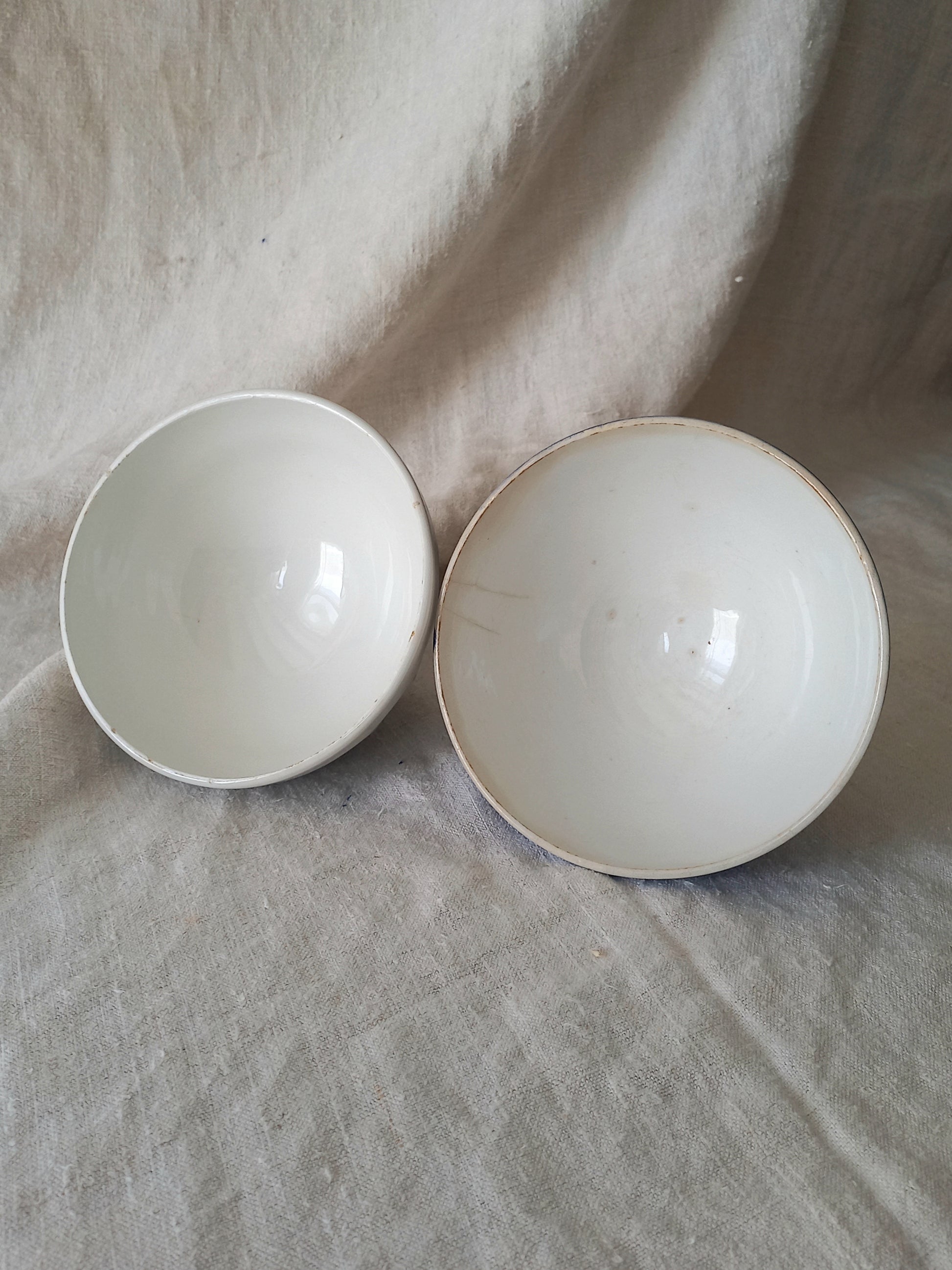 Interiors of blue and white vintage ceramic cafe au lait bowls on a light fabric background.