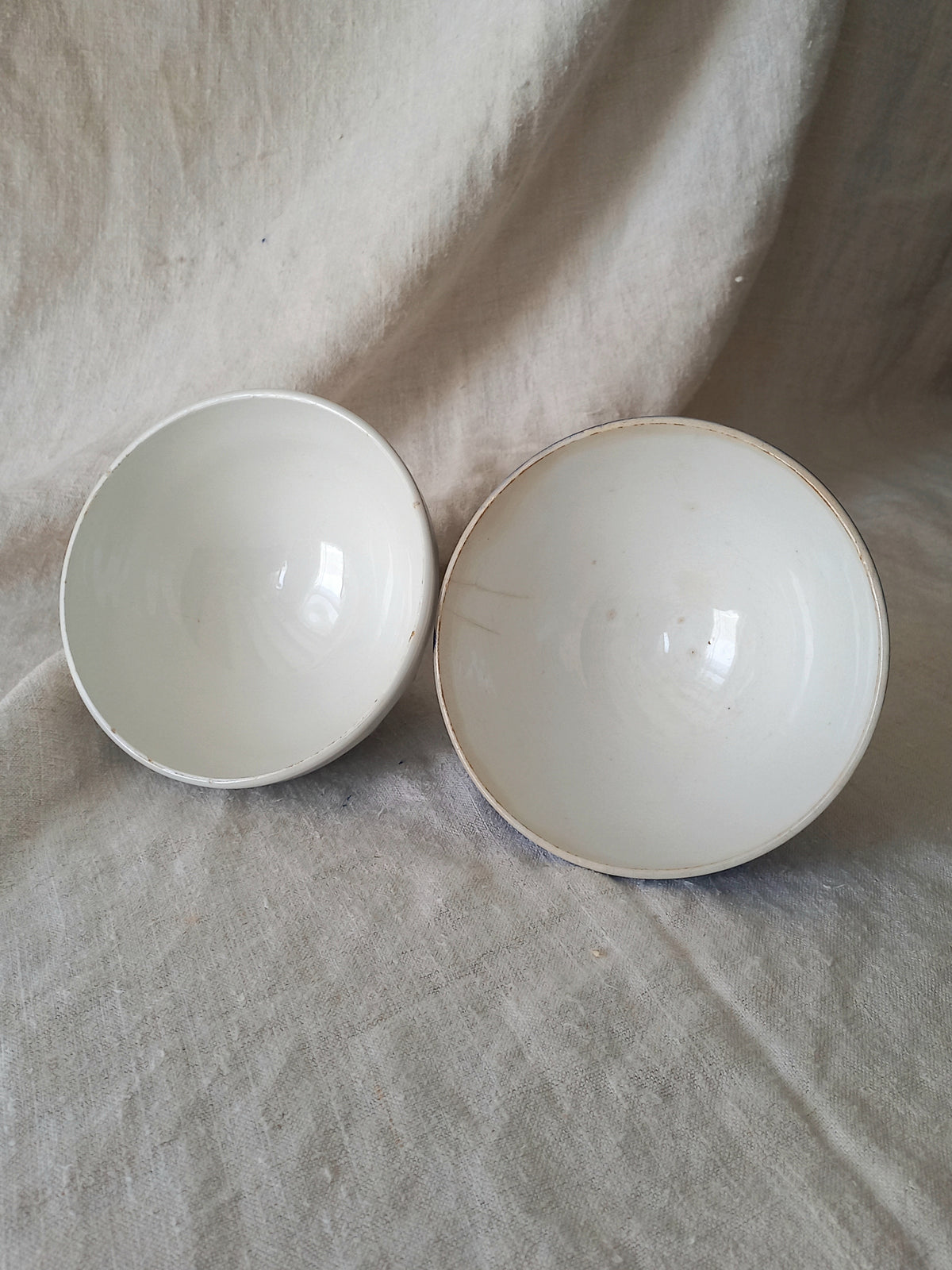 Interiors of blue and white vintage ceramic cafe au lait bowls on a light fabric background.