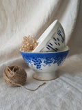 Blue and white vintage ceramic cafe au lait bowls with floral patterns on a light fabric background.