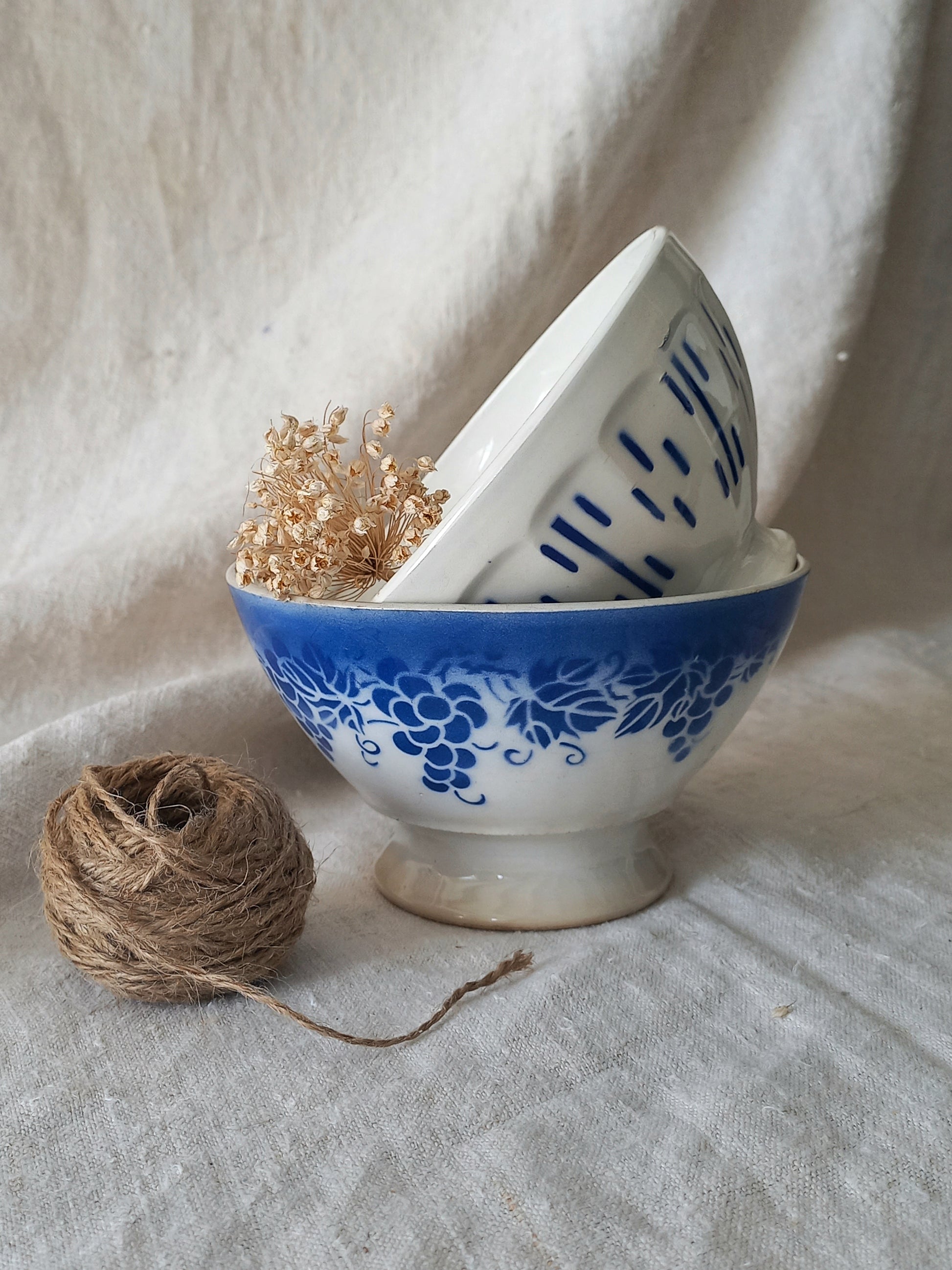 Blue and white vintage ceramic cafe au lait bowls with floral patterns on a light fabric background.