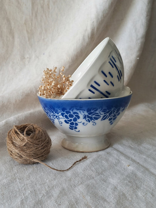Blue and white vintage ceramic cafe au lait bowls with floral patterns on a light fabric background.