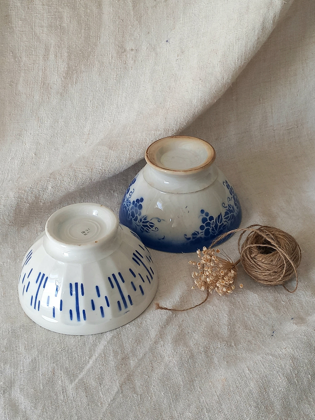 Blue and white vintage ceramic cafe au lait bowls with floral patterns on a light fabric background.