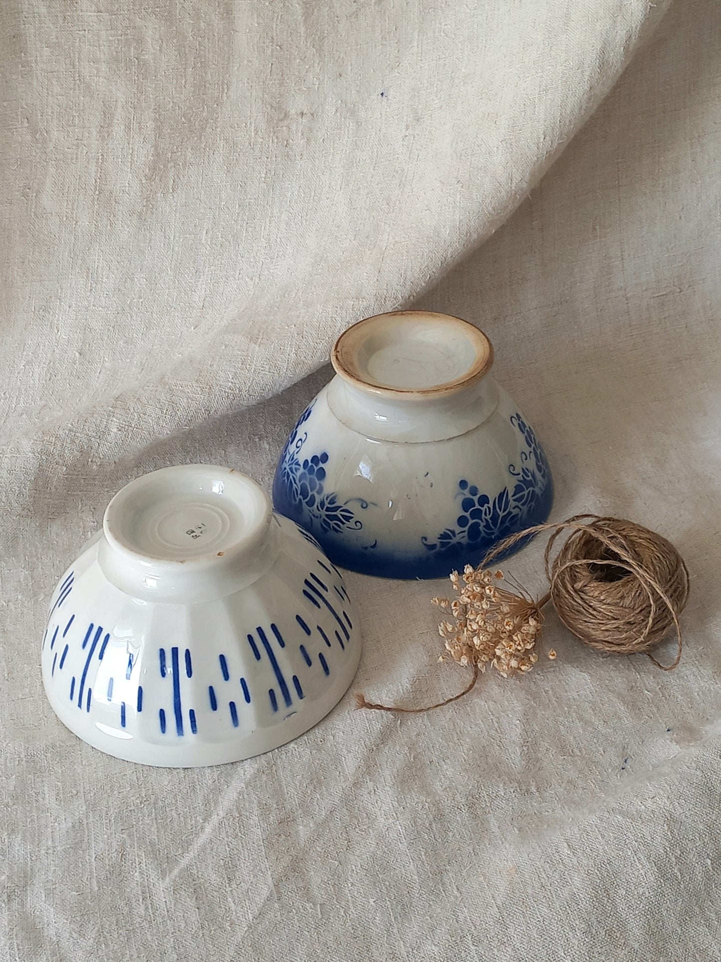 Blue and white vintage ceramic cafe au lait bowls with floral patterns on a light fabric background.