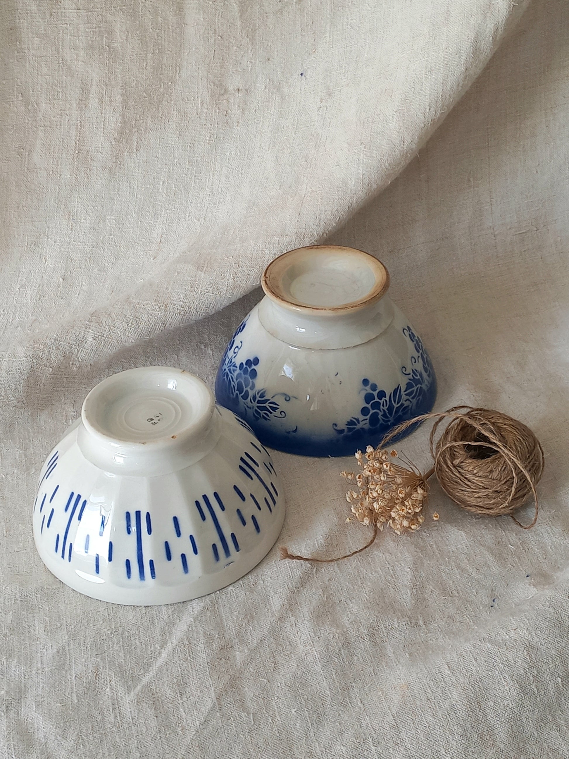 Blue and white vintage ceramic cafe au lait bowls with floral patterns on a light fabric background.