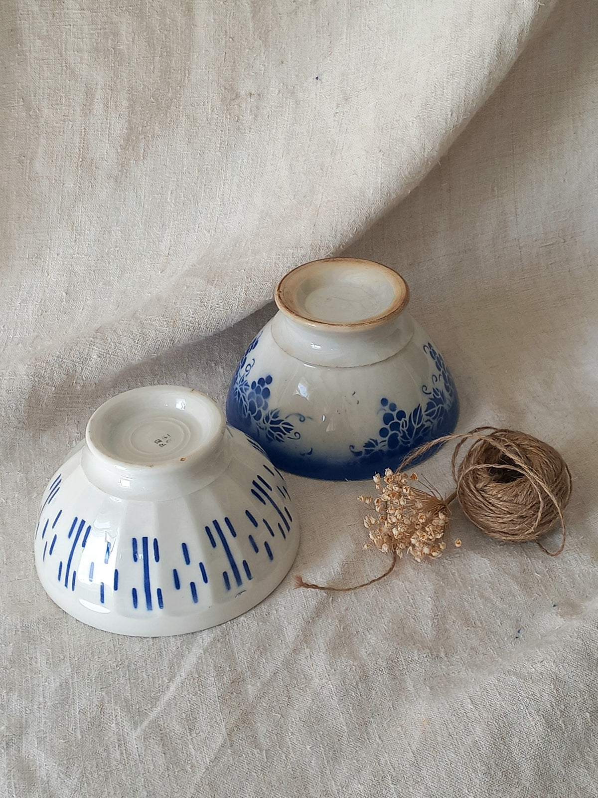 Blue and white vintage ceramic cafe au lait bowls with floral patterns on a light fabric background.