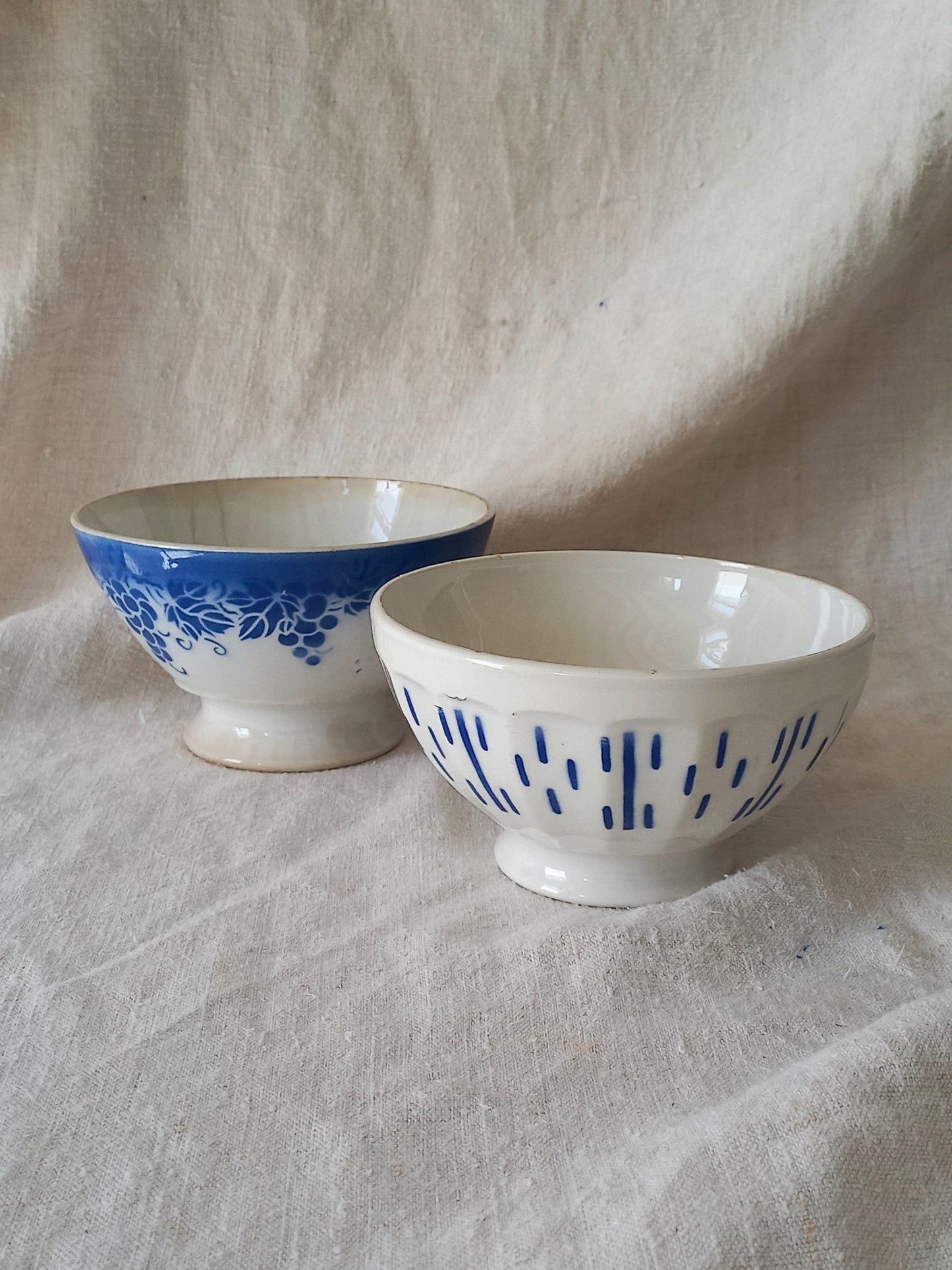 Blue and white vintage ceramic cafe au lait bowls with floral patterns on a light fabric background.